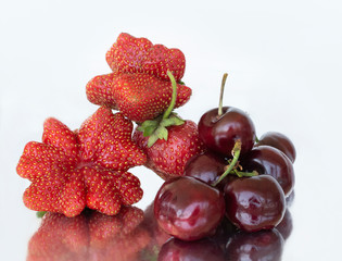 Strawberries of non-standard shapes and cherries on a white background and their reflection in foil.