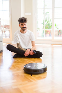 Young man using automatic vacuum cleaner to clean the floor, controling machine housework robot