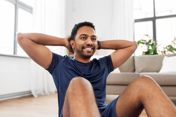sport, fitness and healthy lifestyle concept - smiling indian man making abdominal exercises at home