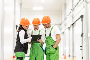 Team of workers in protective workwear discussing and looking a t clipboard indoors.
