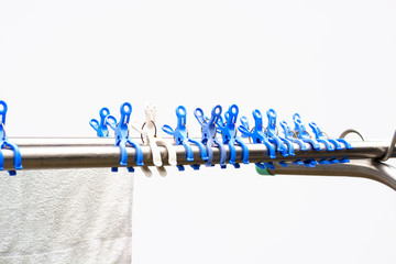 View on a row of blue and white plastic clothespins or clothes pegs, meant for drying laundry outdoors in the wind. To make the wet clothes fresh and soft. The pins are fastened on a shiny metal bar