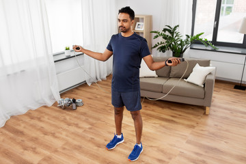 Fototapeta na wymiar fitness, sport, exercising and healthy lifestyle concept - indian man skipping with jump rope at home