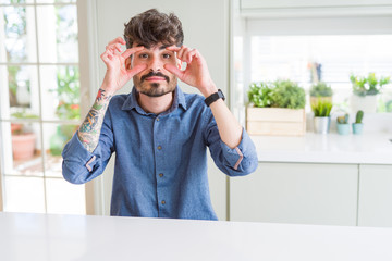 Young man wearing casual shirt sitting on white table Trying to open eyes with fingers, sleepy and tired for morning fatigue