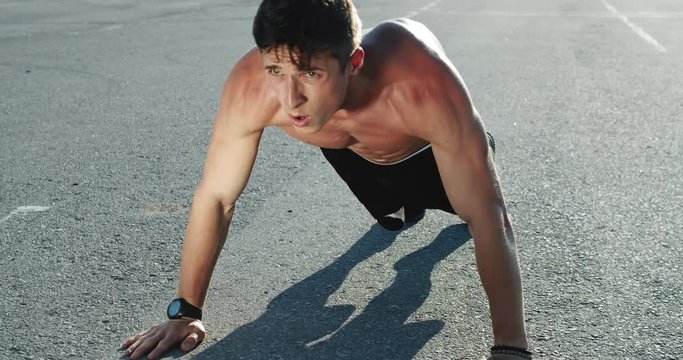 Determined young man making sports exercises outdoors, maintaining muscular posture.