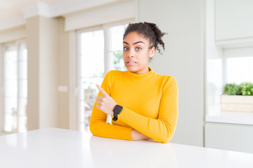 Fototapeta na wymiar Beautiful african american woman with afro hair wearing a casual yellow sweater Pointing aside worried and nervous with forefinger, concerned and surprised expression