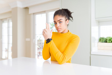 Beautiful african american woman with afro hair wearing a casual yellow sweater Holding symbolic gun with hand gesture, playing killing shooting weapons, angry face