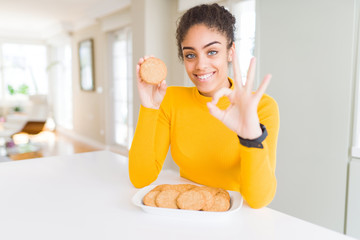 Young african american girl eating healthy whole grain biscuits doing ok sign with fingers, excellent symbol