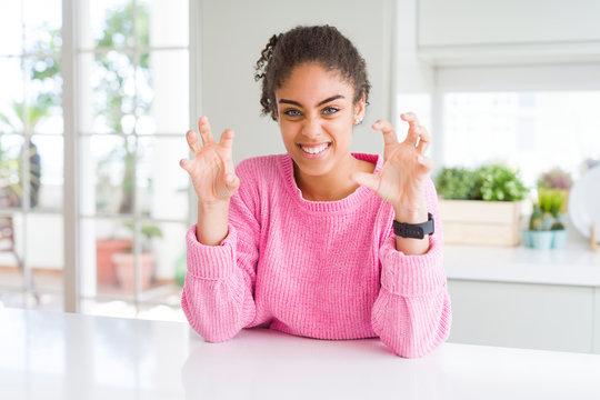 Beautiful african american woman with afro hair wearing casual pink sweater smiling funny doing claw gesture as cat, aggressive and sexy expression