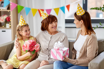 family, generation and celebration concept - smiling mother with gift box and daughter with flowers...