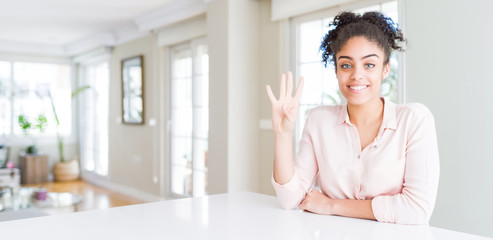 Wide angle of beautiful african american woman with afro hair showing and pointing up with fingers number four while smiling confident and happy.