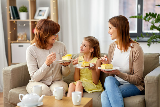 family, generation and food concept - smiling mother, daughter and grandmother having tea party and eating cake at home