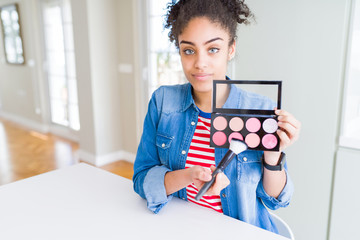 Young african american woman holding cosmetics blush palette with a confident expression on smart...