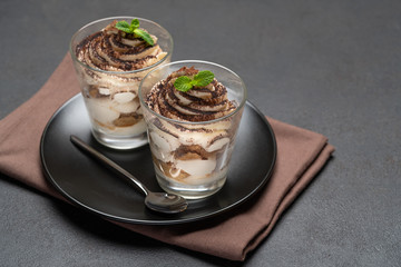Classic tiramisu dessert in a glass on dark concrete background