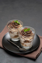 Classic tiramisu dessert in a glass on dark concrete background