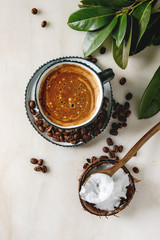 Bulletproof coffee. Keto diet coffee in blue ceramic cup with organic coconut cold press oil in wooden spoon with beans and green branch over white marble background. Flat lay, space