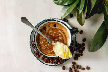 Bulletproof coffee. Keto diet coffee in blue ceramic cup with organic ghee butter in spoon with beans and green branch over white marble background. Flat lay, space