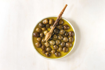 Ceramic plate of green whole olives in olive oil over white marble background. Flat lay, space