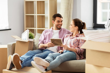 moving, people, repair and real estate concept - happy couple with photo frame and cardboard boxes sitting on sofa at new home