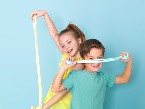 Cool, Pretty Boy And His Older Sister Are Playing With Homemade Slime In Front Of A Blue Background And Having A Lot Of Fun And Are Laughing