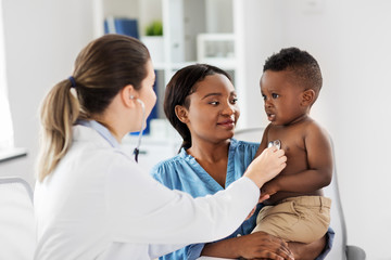 Obraz premium medicine, healthcare and pediatry concept - doctor with stethoscope listening to african american baby boy on medical exam at clinic