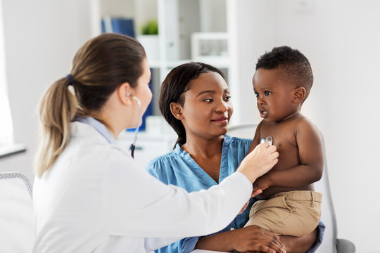 medicine, healthcare and pediatry concept - doctor with stethoscope listening to african american baby boy on medical exam at clinic
