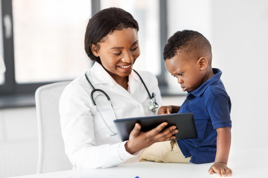 medicine, healtcare, pediatry and people concept - happy african american female doctor or pediatrician showing tablet computer to baby boy patient at clinic