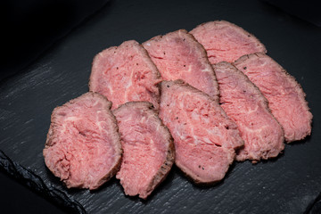 Sliced Grass Fed Juicy Corn Roast Beef on black natural stone background.