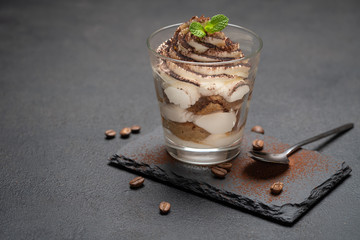 Classic tiramisu dessert in a glass on stone serving board on dark concrete background