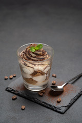 Classic tiramisu dessert in a glass on stone serving board on dark concrete background