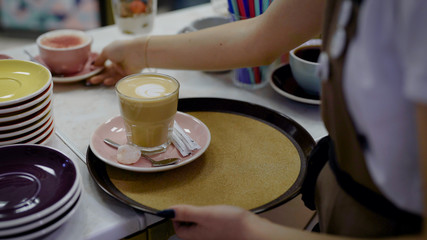 female waiter is putting dessert and two mugs with sweet coffee on a round tray and carrying it over cafe hall