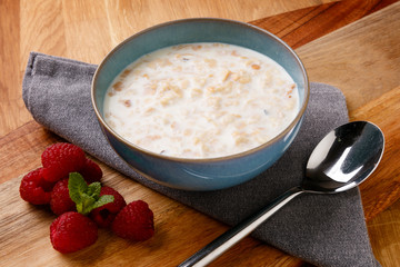 Delicious bowl of porridge and raspberrys shot on a wooden board with a napkin and spoon.