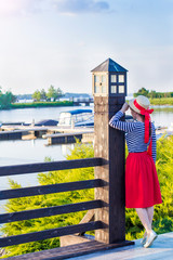 Beautiful girl in a straw hat on the pier near the sea yachts and boats. Girl in a red skirt and a sailor suit on the pier at sunset on vacation