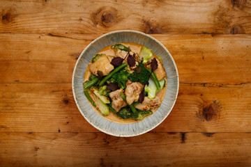 A bowl of succulent Thai Red Chicken Curry shot a wooden background