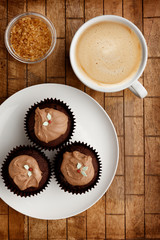 Chocolate fairy cakes and a cup of coffee with brown sugar on a wooden background