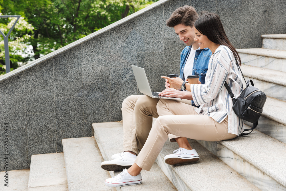 Wall mural Amazing loving couple business people colleagues outdoors outside on steps using laptop computer drinking coffee.