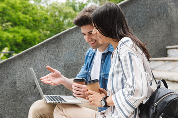 Amazing loving couple business people colleagues outdoors outside on steps using laptop computer drinking coffee.