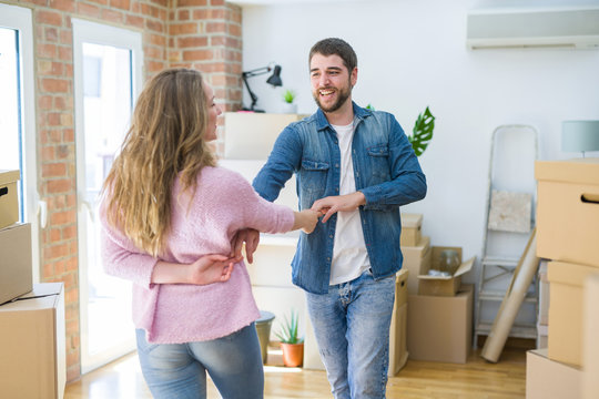 Young couple dancing celebrating moving to new apartment around cardboard boxes