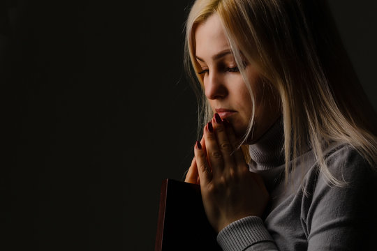 A Woman Is Holding And Hug The Bible At Her Chest In The Morning. Bible Is Black Cover.