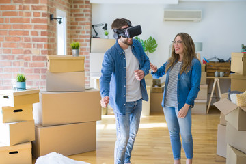 Fototapeta na wymiar Young couple moving to a new house having fun playing with virtual reality glasses around cardboard boxes