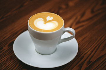 Cup of coffee with latte art on wooden background.