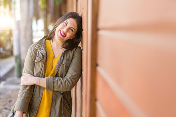 Beautiful young woman smiling confident and cheerful leaning on wooden wall, walking on the street of the city on a sunny day