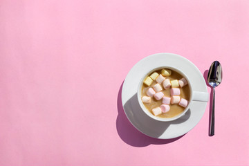 Cup of hot cocoa/coffee with marshmallows on pink table, top view, flat lay