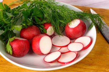 Radish, dill and parsley on a white plate. The plate and the knife on the Board