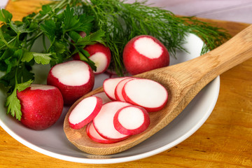 Dill, radishes and parsley in a bowl. Chopped radish in a wooden spoon