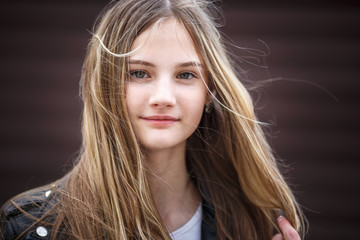 Fototapeta premium close-up portrait of little beautiful stylish kid girl with long flowing hair against a brown striped wall