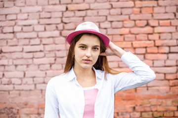 close up portrait of beautiful stylish kid girl in hat near pink brick wall as background