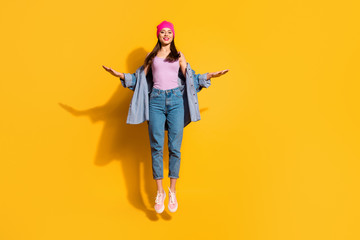 Full length body size photo beautiful she her lady hands arms raised sides air jump high sportive day off amazing look wear casual jeans denim jacket shoes pink hat isolated yellow bright background