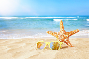 Fototapeta na wymiar holidays. sand beach, sunglasses and starfish in front of summer sea background with copy space