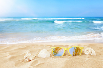 Fototapeta na wymiar Empty sand beach, seashells and sunglasses in front of summer sea background with copy space
