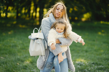 young blonde mother holding her toddler daughter in her arms as they are walking through the park on a sunny day